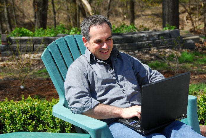 Man smiling while working remotely on a laptop outdoors in a garden setting