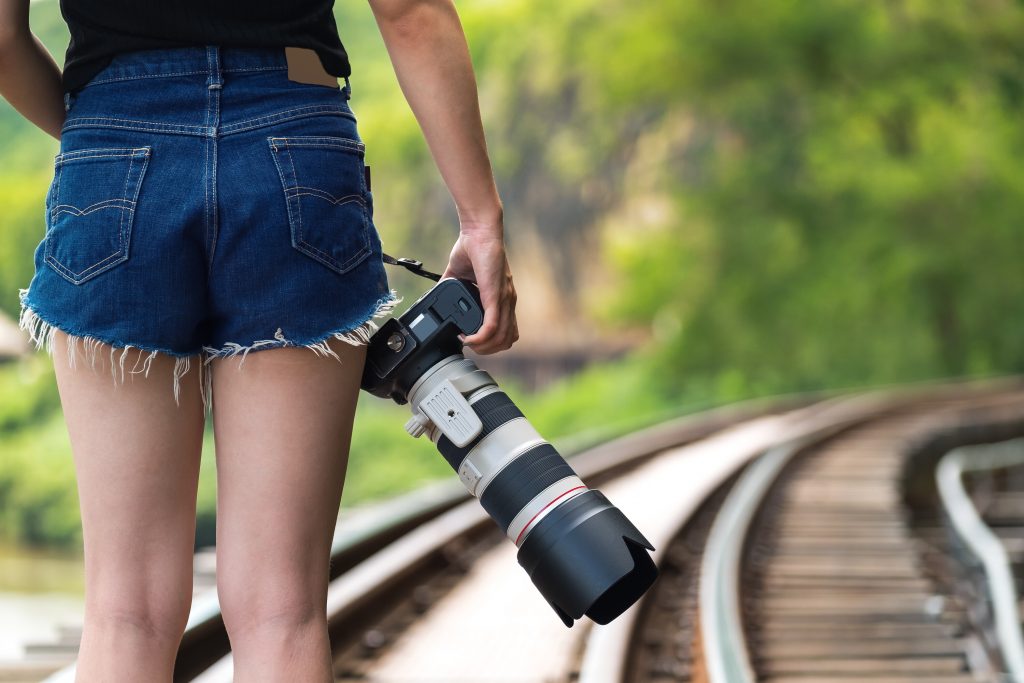 Person holding a professional camera while standing on railway tracks, symbolizing the freedom to escape the 9-5 grind