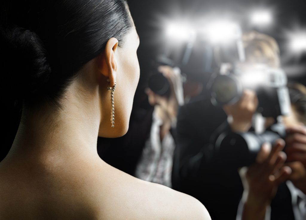 Back view of a woman facing paparazzi with flashing cameras, symbolizing the attention and publicity involved in becoming a public figure or influencer