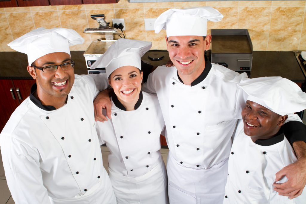 A group of chefs in a kitchen smiling and ready to start their catering side hustle