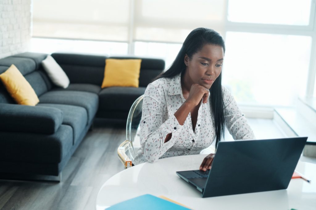 Woman working remotely on a laptop from home, sitting at a modern, well-lit workspace