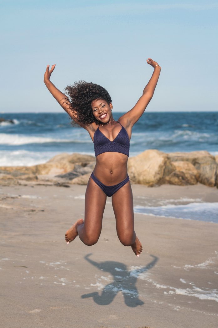 A joyful woman in a bikini jumping on the beach, symbolising the freedom and energy of being a personal trainer