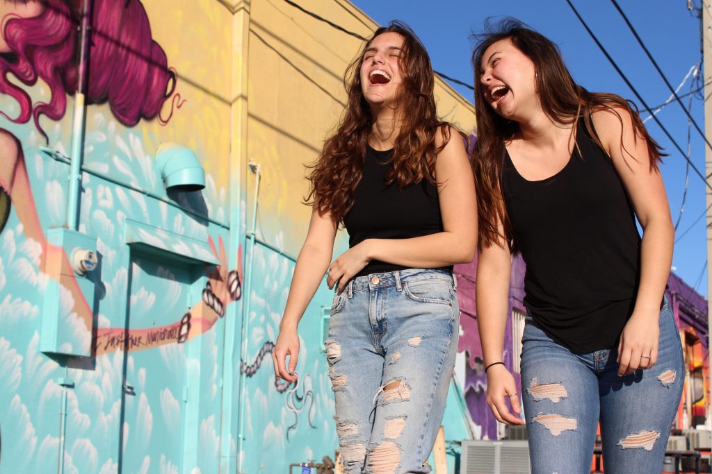 Two young women laughing and walking in front of a colourful mural, symbolising the freedom and flexibility of the gig economy