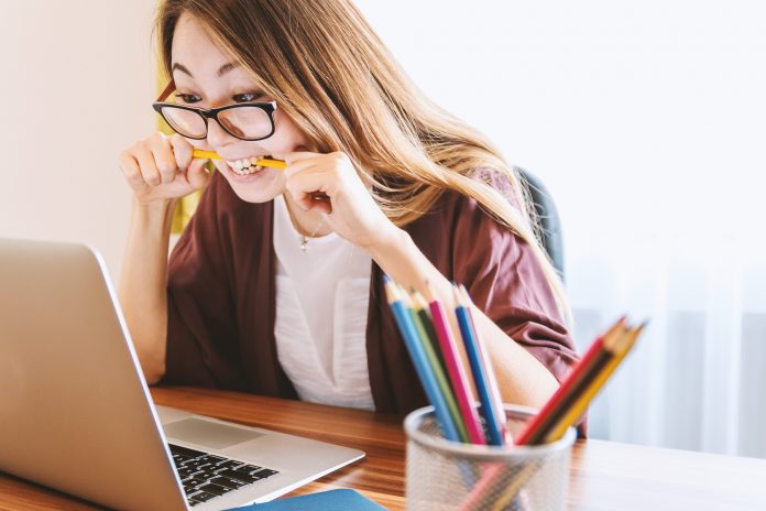 Woman biting a pencil while working on a laptop, symbolizsng the effort and focus required to create a winning proposal for freelance projects