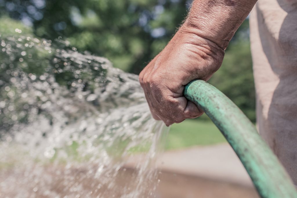 Close-up of a person holding a hose, watering plants, representing the landscape gardening business