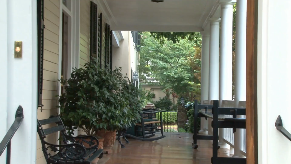 A charming front porch of a house with plants and rocking chairs, representing a cozy Airbnb hosting setup in the UK