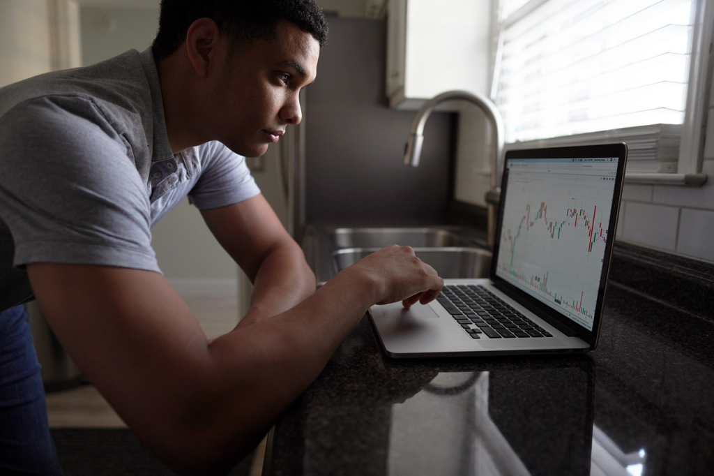 Focused individual analysing Forex trading charts on a laptop in a home setting