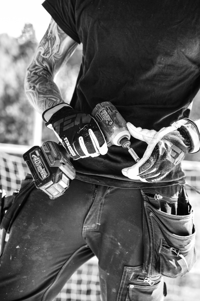 A black-and-white close-up of a handyman wearing gloves and holding a power drill, representing the practical skills required in the handyman business